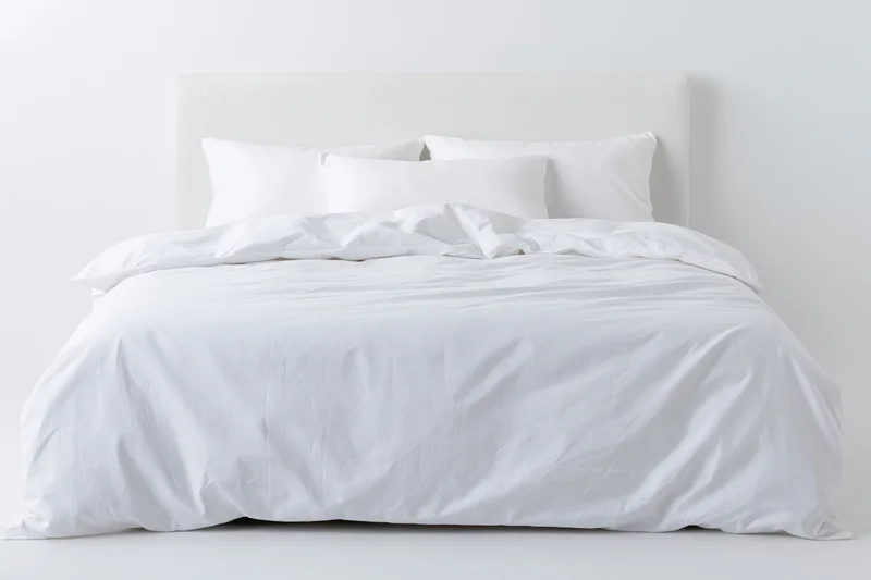 White bed with crumpled duvet and pillows against plain white background