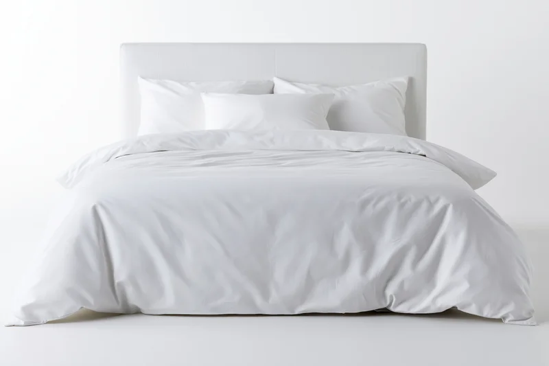 White double bed with cotton duvet and pillows against plain white background