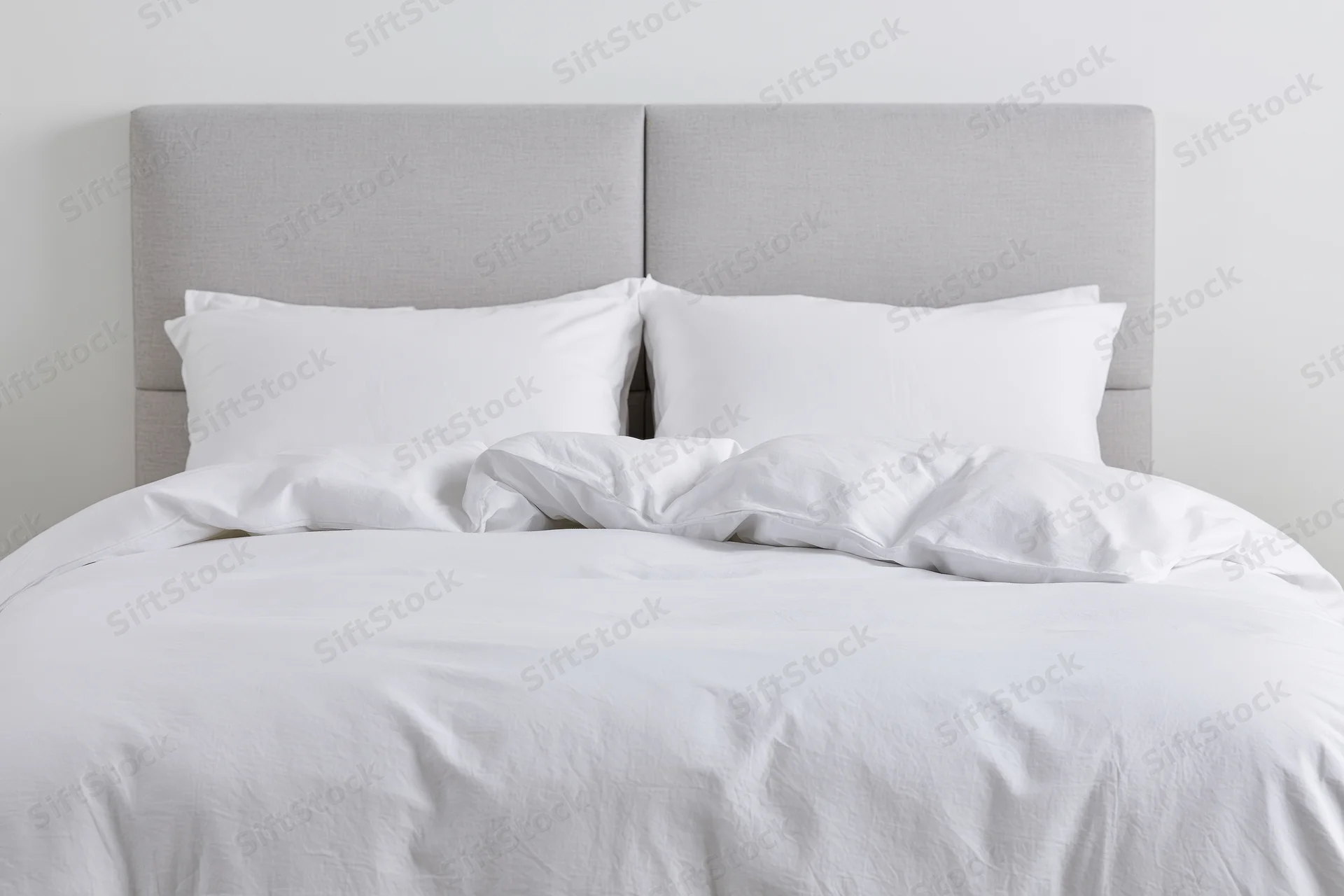 Double bed with white bedding and gray headboard in a minimalist bedroom