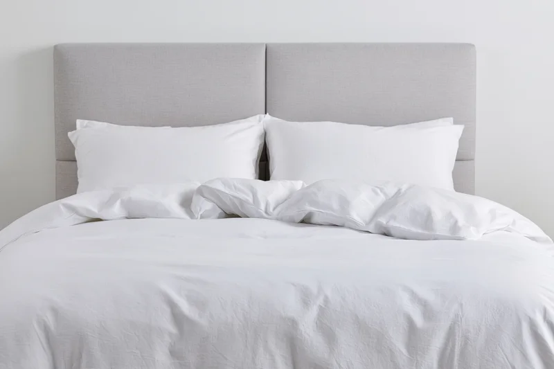 Double bed with white bedding and gray headboard in a minimalist bedroom