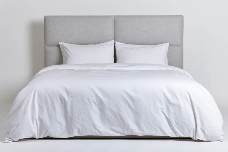 Double bed with white duvet and two white pillows against a gray headboard in a minimalist bedroom setting