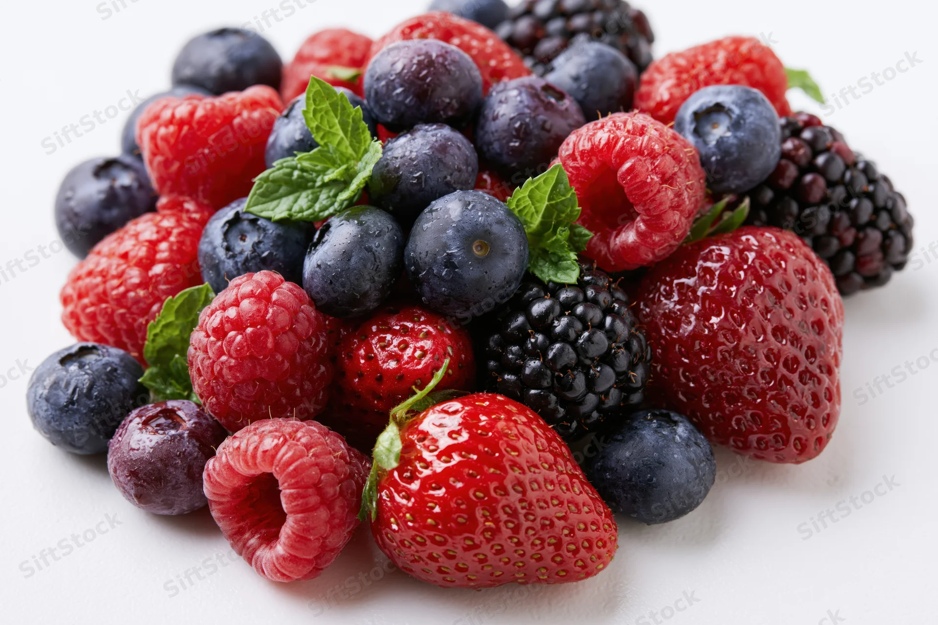 A pile of mixed fresh berries including strawberries, raspberries, blueberries and blackberries on a white surface