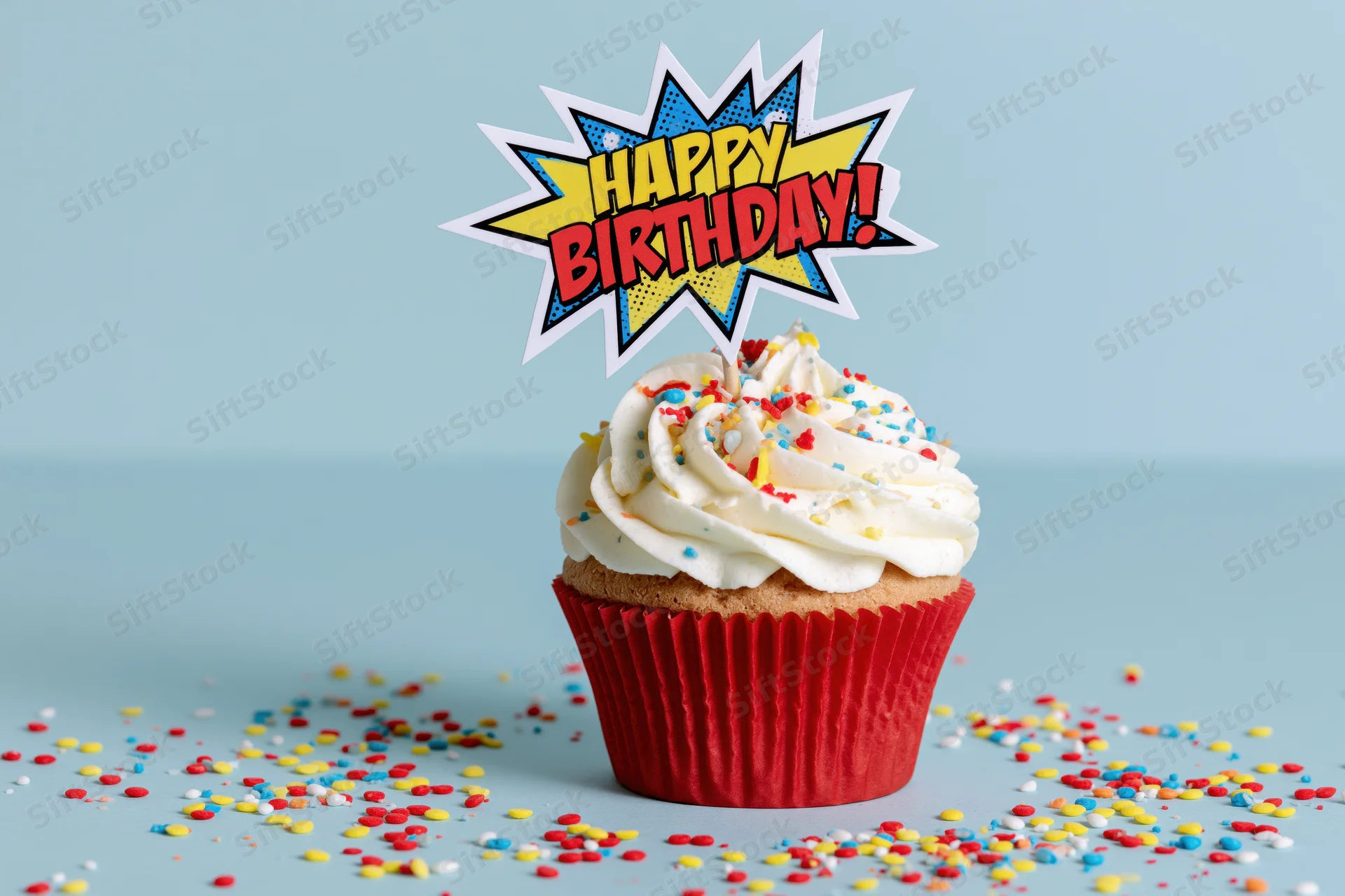 Birthday cupcake with comic-style topper and sprinkles on light blue surface