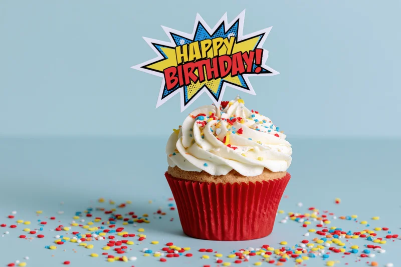 Birthday cupcake with comic-style topper and sprinkles on light blue surface