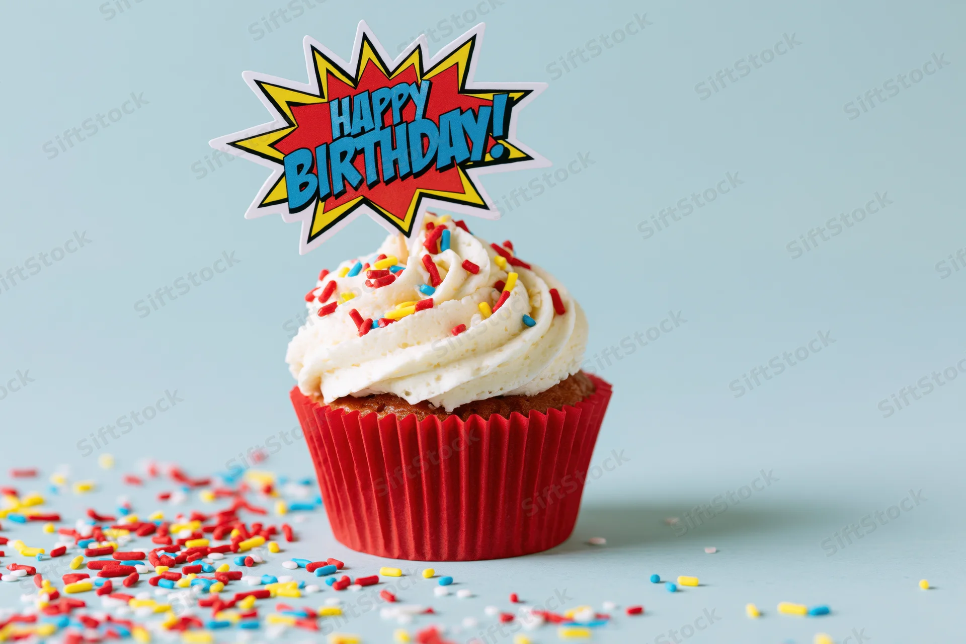 Single birthday cupcake with comic-style topper and sprinkles on light blue surface
