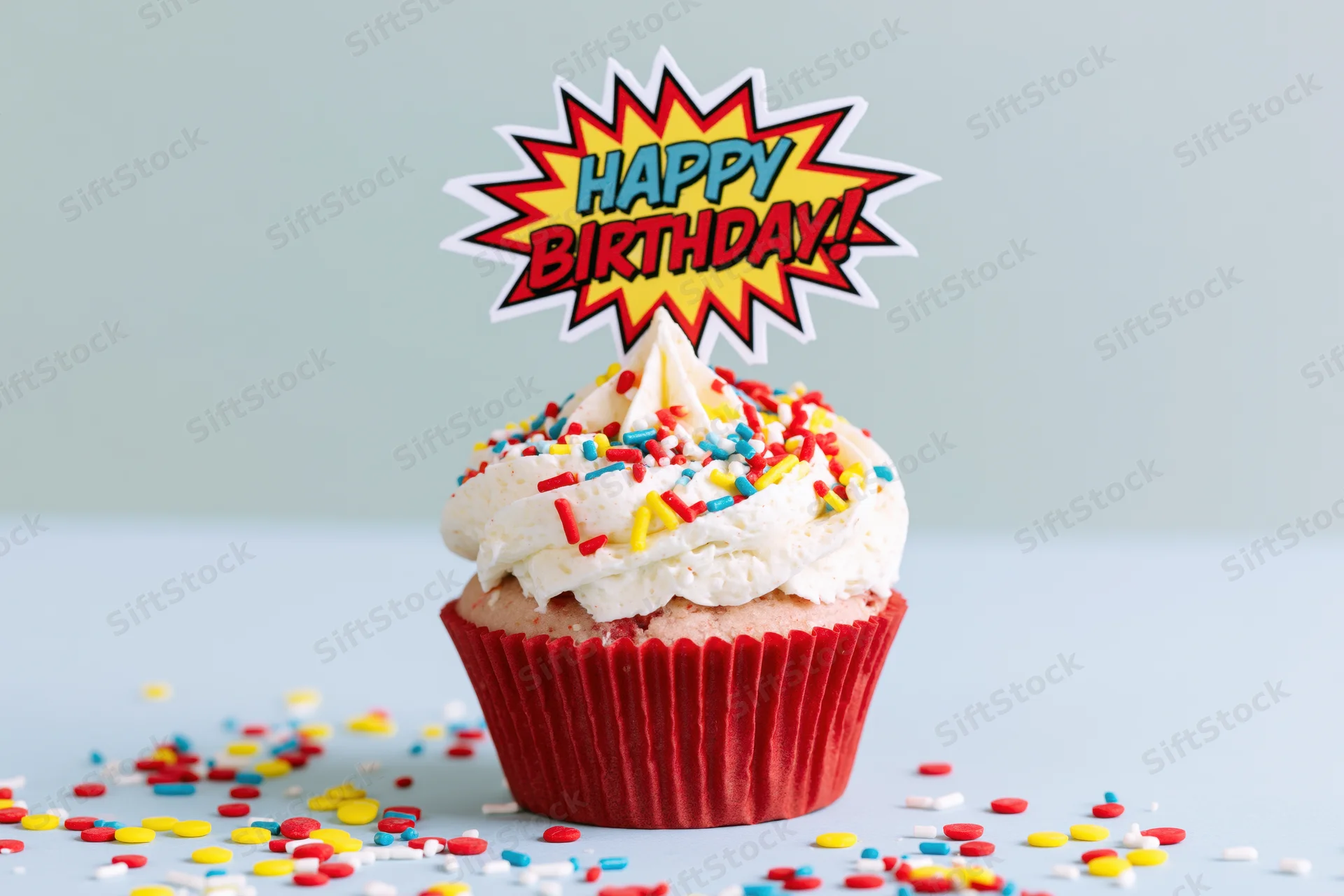 Single birthday cupcake with colorful sprinkles and comic-style topper on light blue surface
