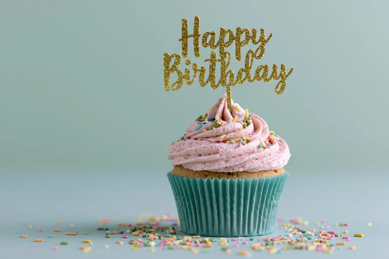 Single birthday cupcake with pink frosting and gold glitter topper in teal paper wrapper on pastel background