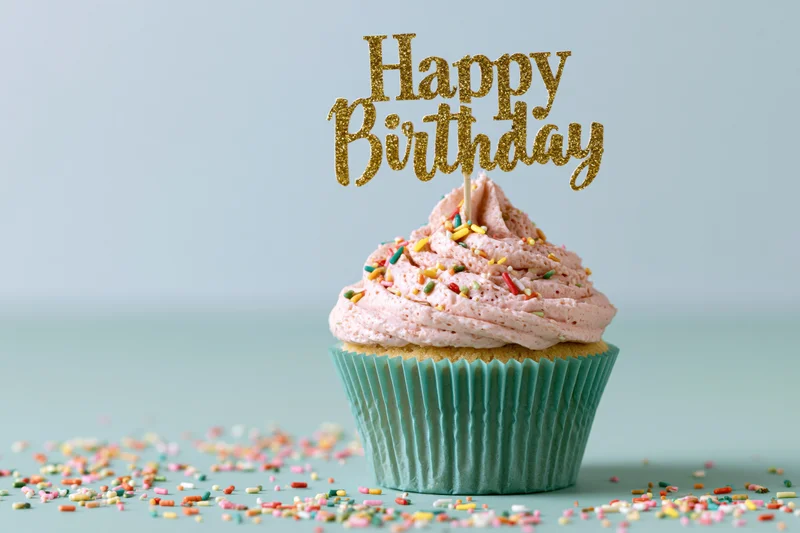 Single birthday cupcake with gold topper and sprinkles on pastel background