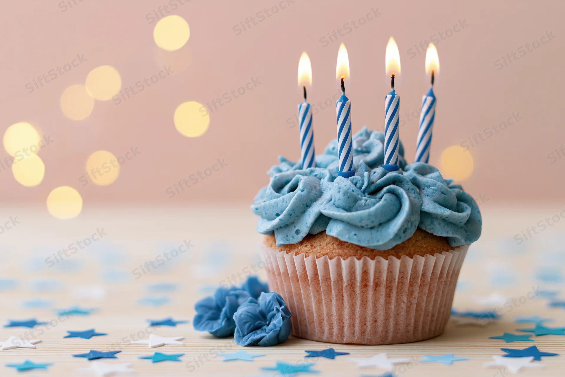 Blue-frosted cupcake with lit candles and star confetti on wooden table