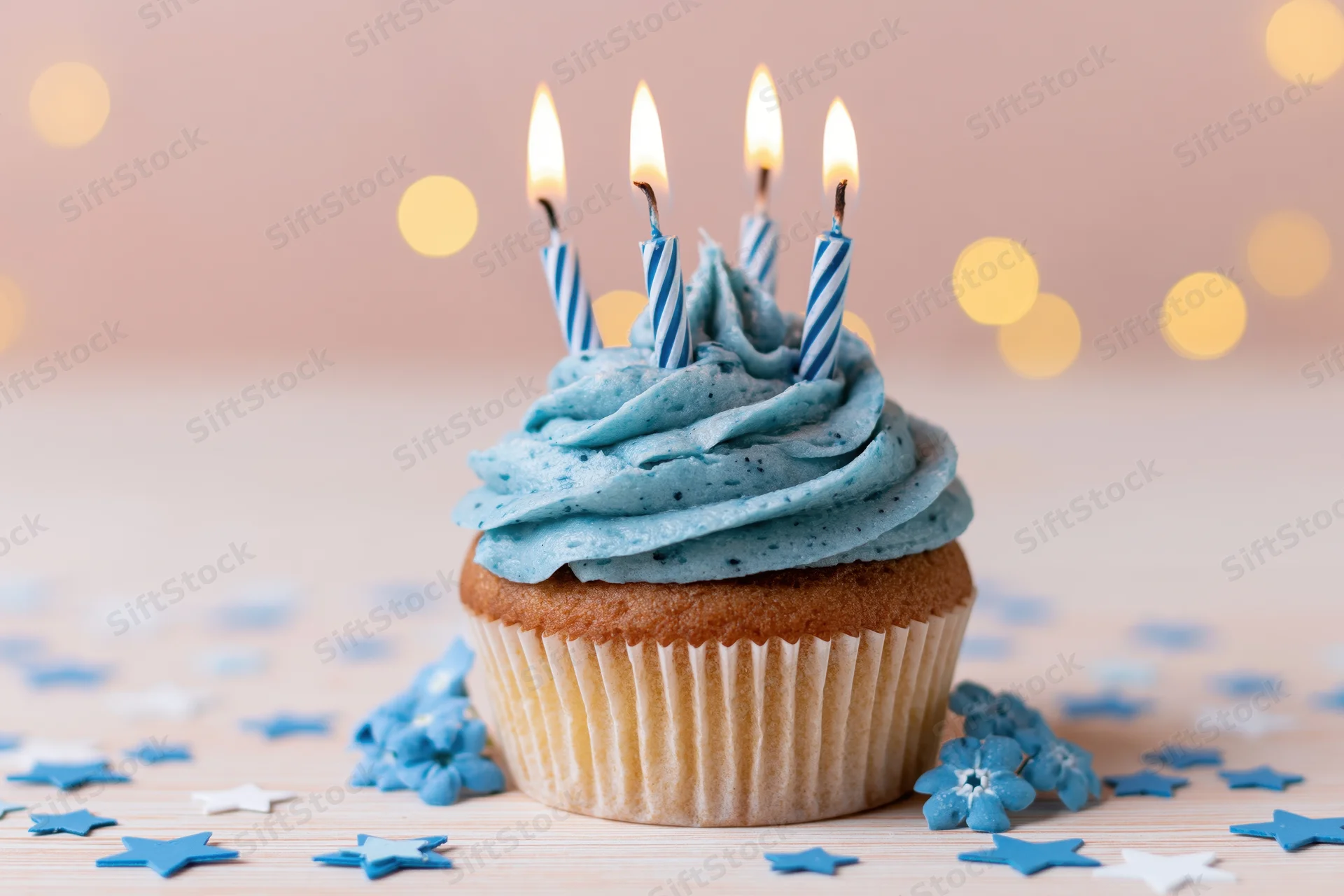 Blue-frosted cupcake with lit candles and star confetti on wooden surface