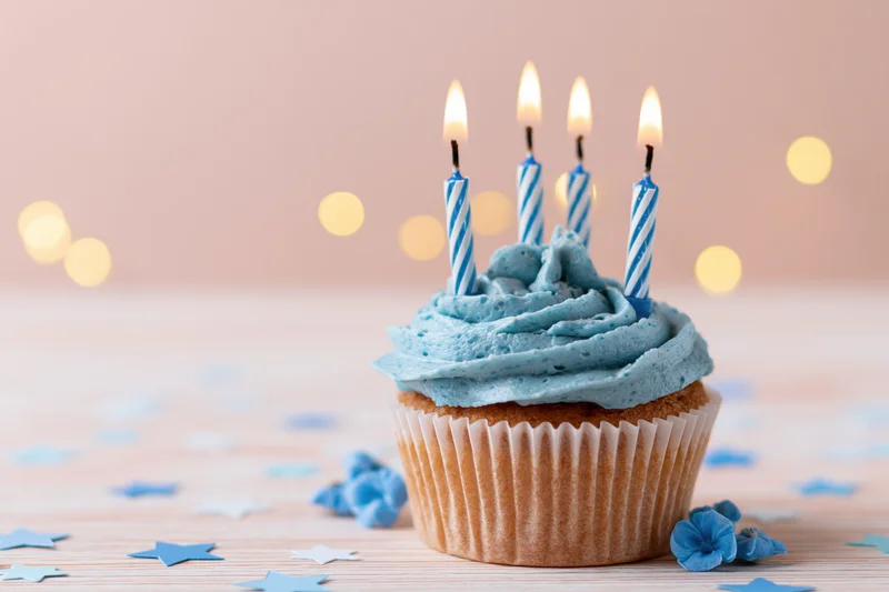Blue-frosted cupcake with lit candles and star confetti on wooden table