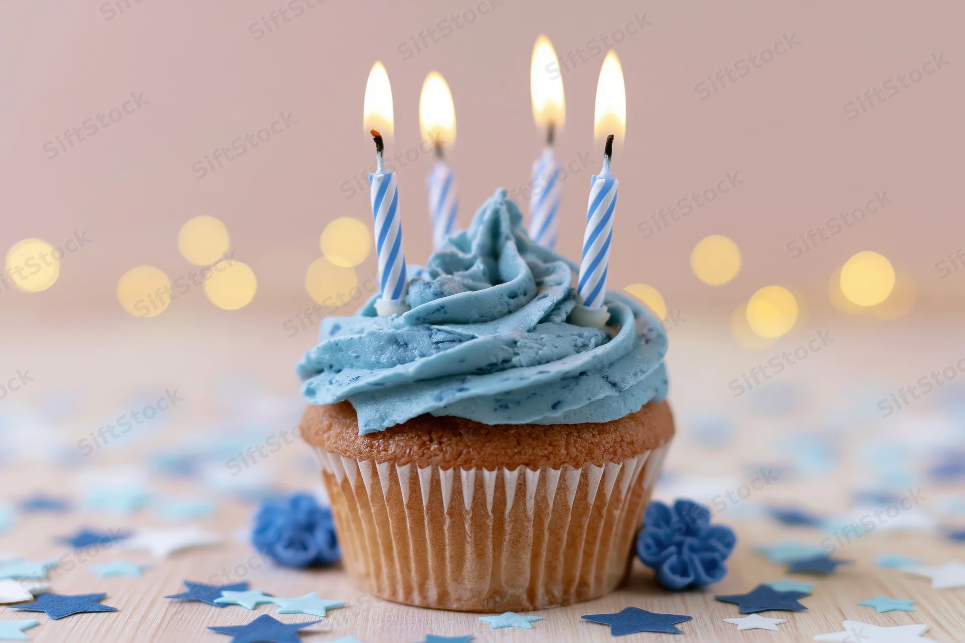 Single birthday cupcake with blue frosting swirl and lit candles on wooden surface with star confetti and bokeh lights