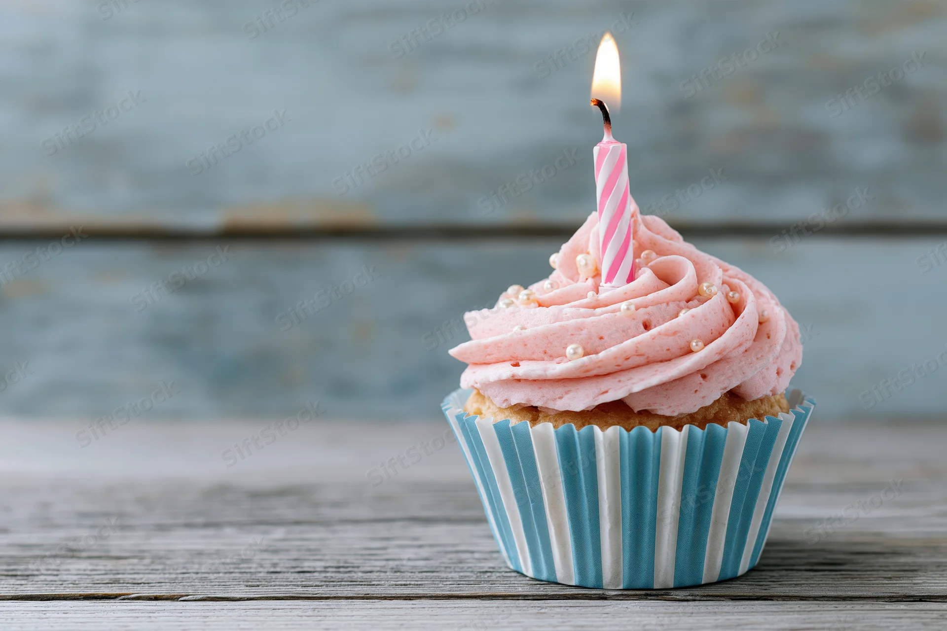 Single birthday cupcake with pink swirled frosting and lit candle on wooden table