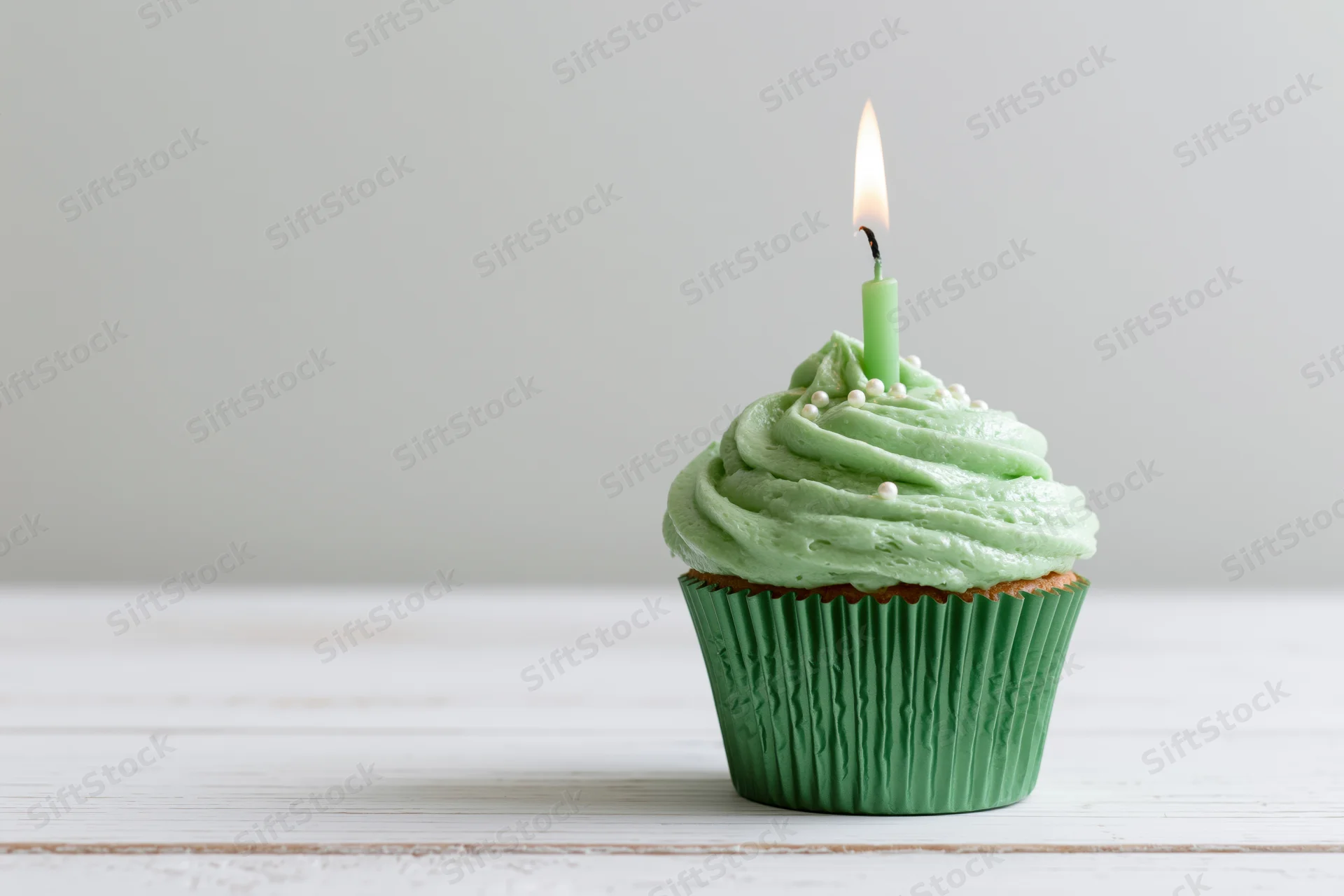 Single green-frosted cupcake with lit candle on white wooden surface