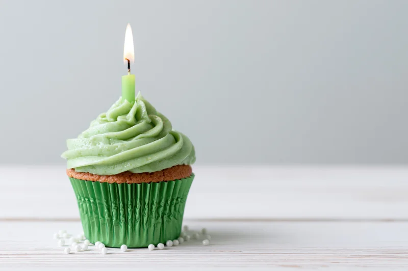 Green frosted cupcake with lit candle on white wooden surface