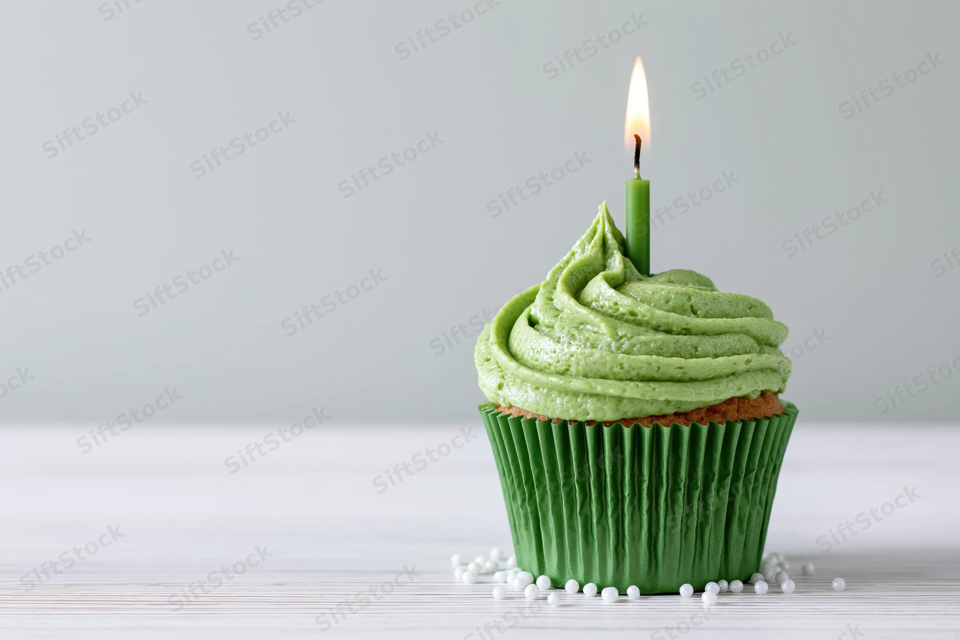 Single green-frosted cupcake with lit candle on white wooden surface