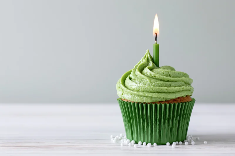 Single green-frosted cupcake with lit candle on white wooden surface