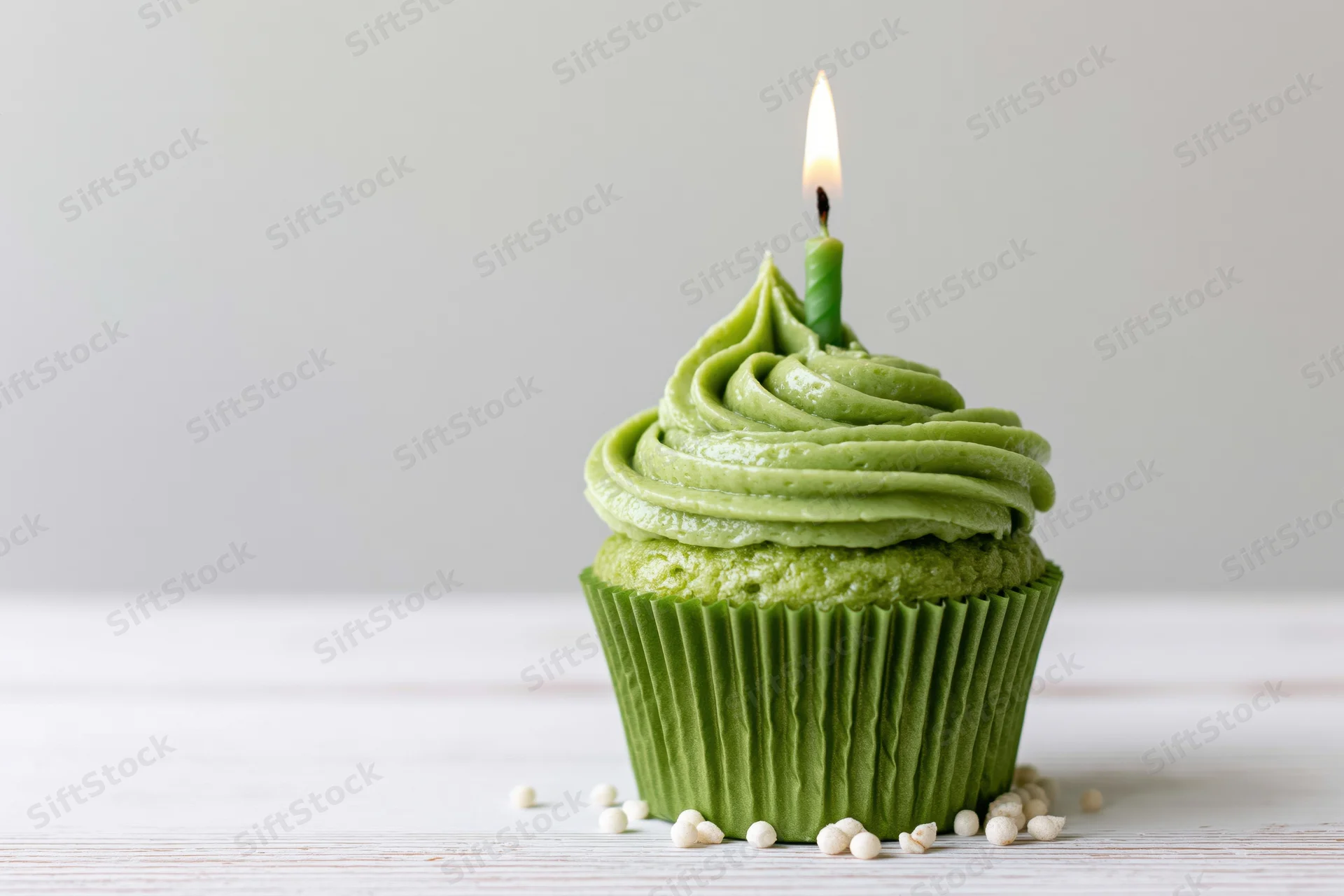 Green frosted cupcake with lit candle on white wooden surface