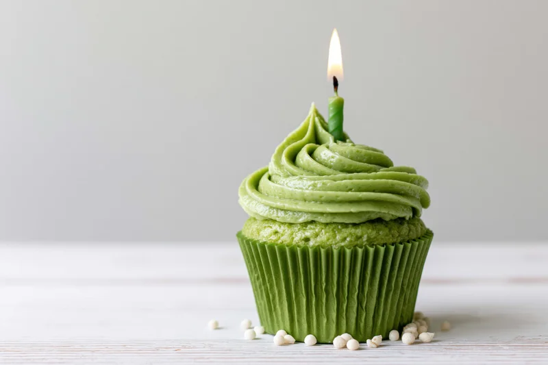 Green frosted cupcake with lit candle on white wooden surface