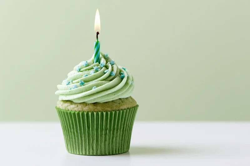 Single green-frosted cupcake with lit candle on white surface