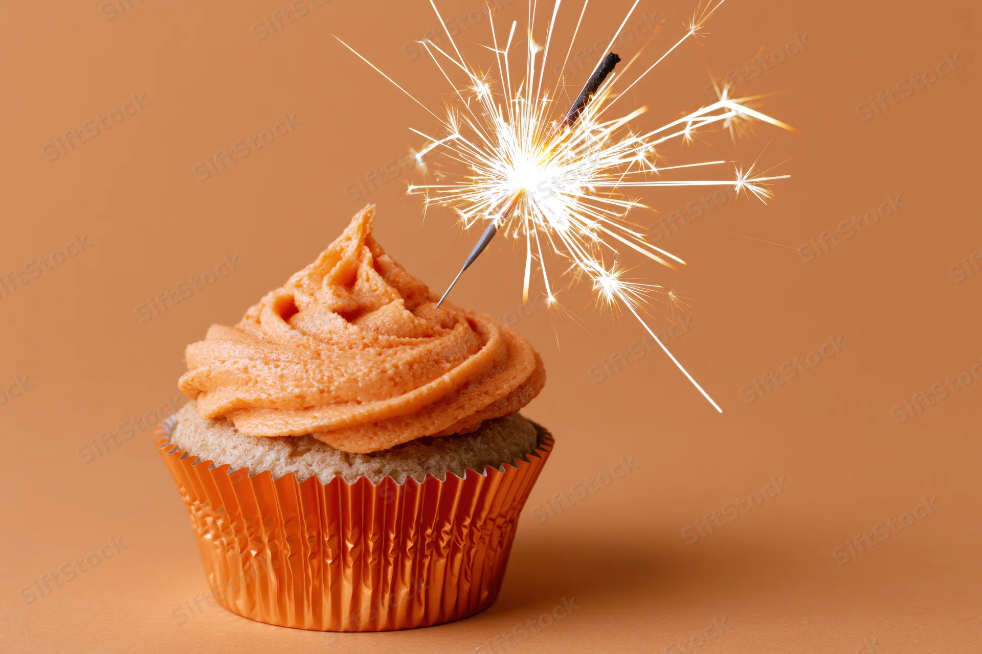Single birthday cupcake with orange frosting and sparkler on warm background