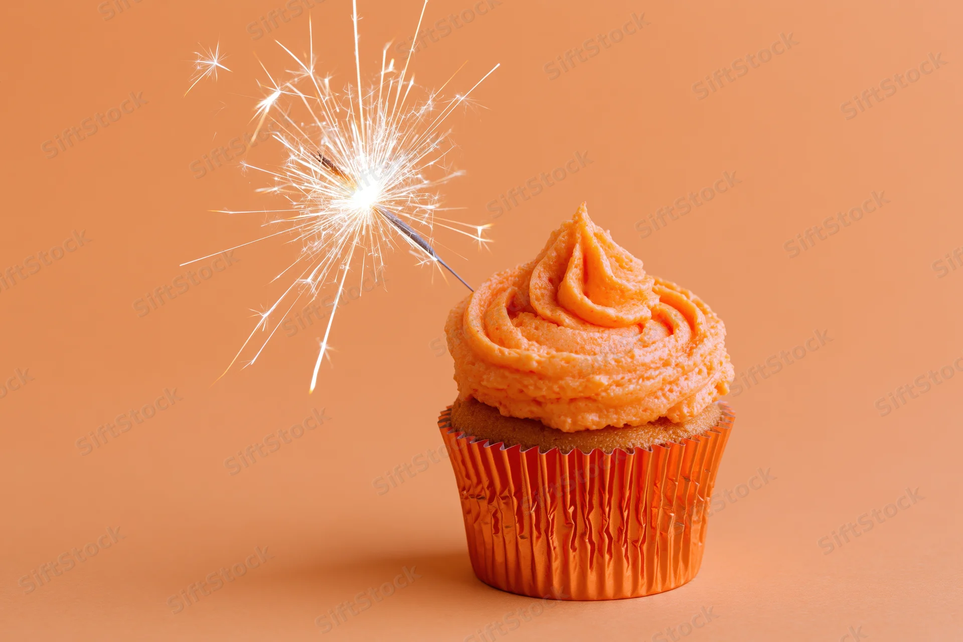 Orange-frosted cupcake with sparkler on solid background