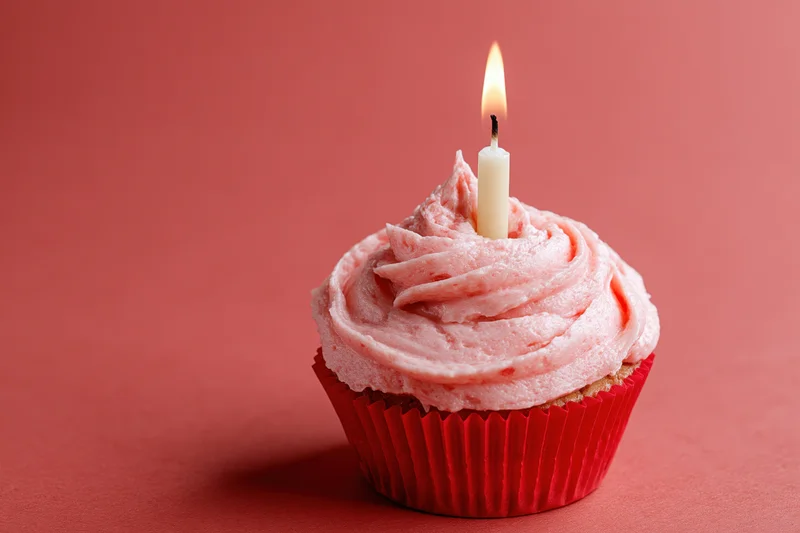 Single birthday cupcake with pink frosting and lit candle on red background