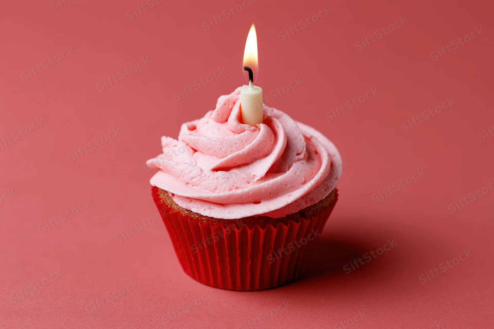 Single birthday cupcake with pink frosting and lit candle on red background