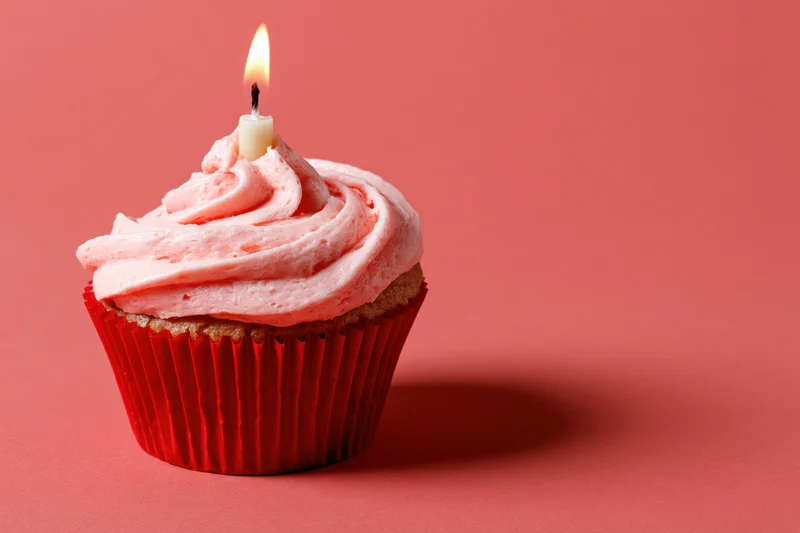 Single birthday cupcake with pink frosting and lit candle on red background