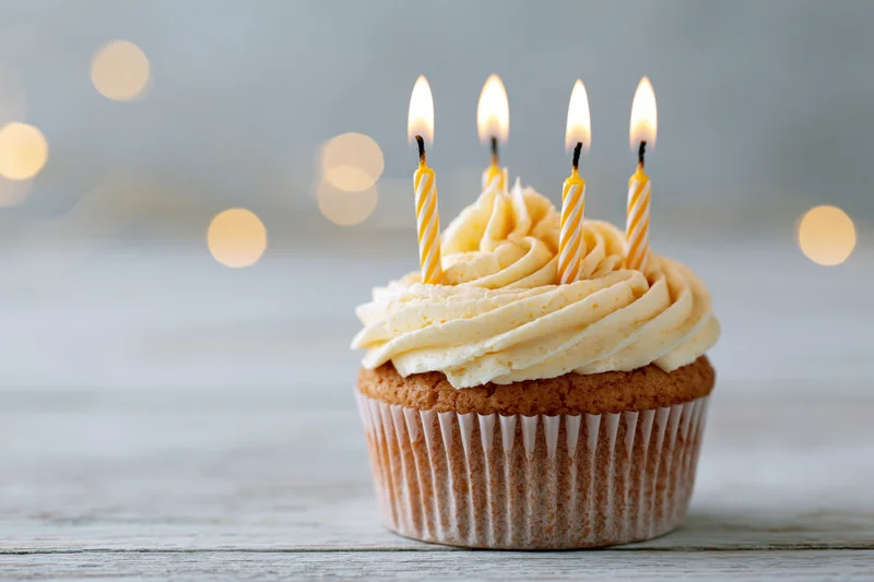 Single birthday cupcake with lit candles and swirled vanilla buttercream on wooden surface
