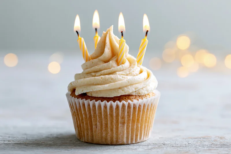 Single birthday cupcake with swirled vanilla buttercream frosting and lit candles on a wooden surface