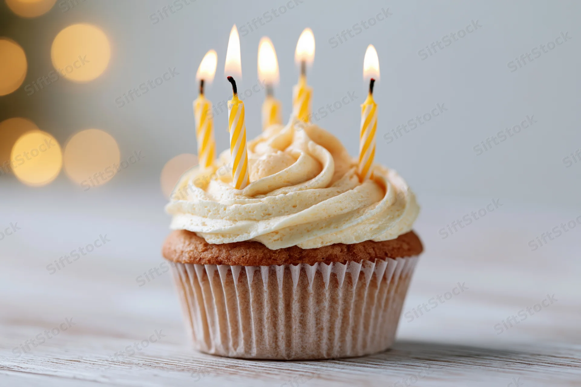 Single birthday cupcake with lit yellow striped candles and swirled vanilla buttercream on wooden table