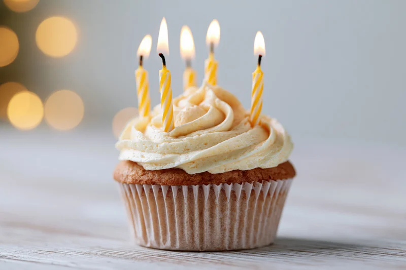 Single birthday cupcake with lit yellow striped candles and swirled vanilla buttercream on wooden table