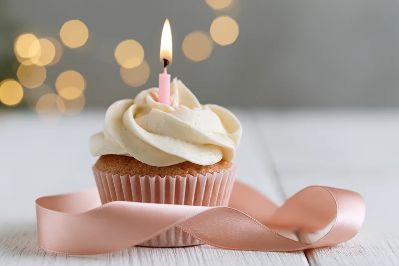 Birthday cupcake with lit candle and pink ribbon on wooden surface