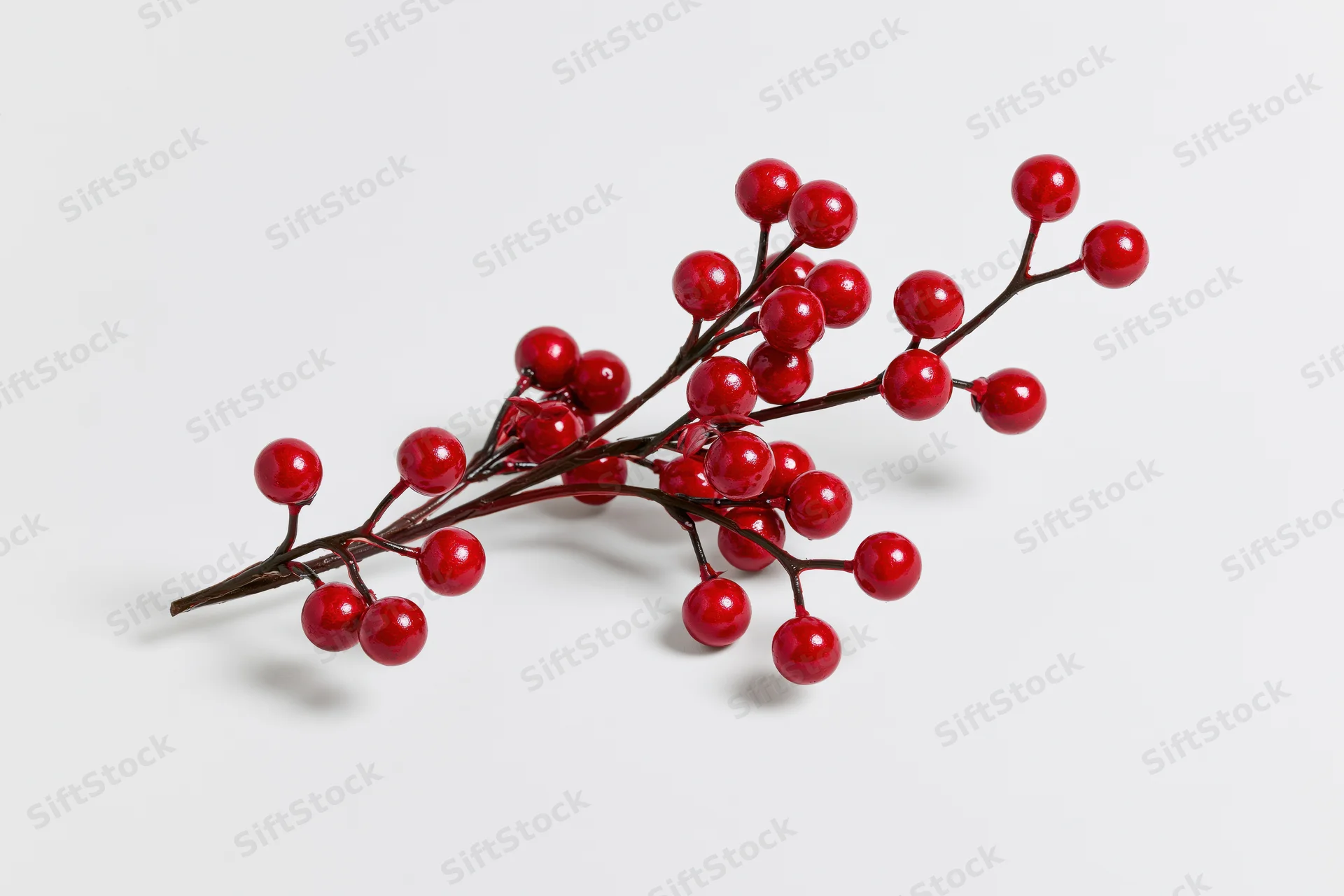 Artificial holly branch with glossy red berries on white background