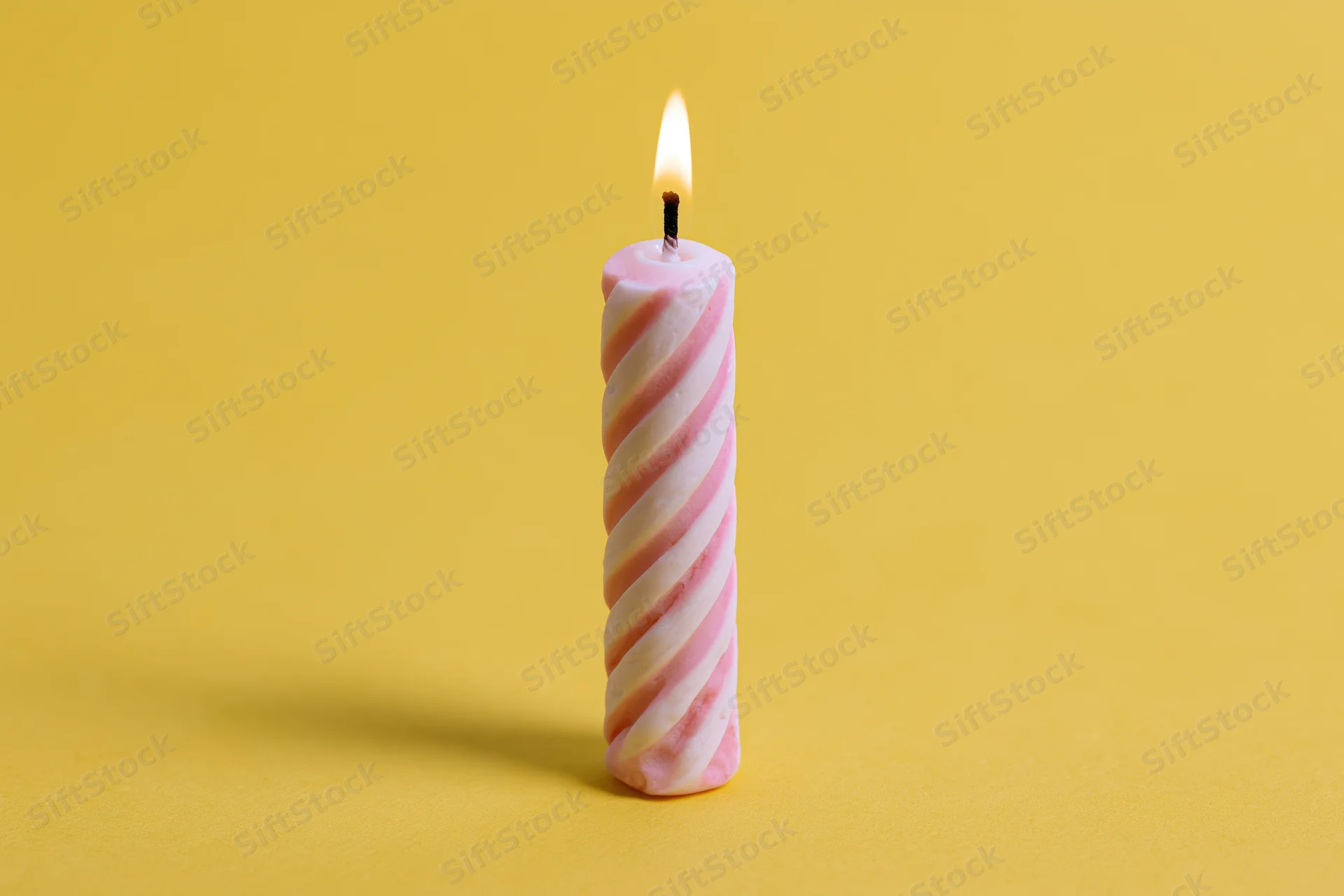 Single lit pink and white spiral birthday candle on yellow background