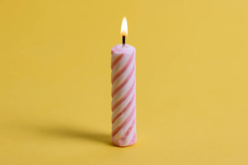 Single lit pink and white spiral birthday candle on yellow background