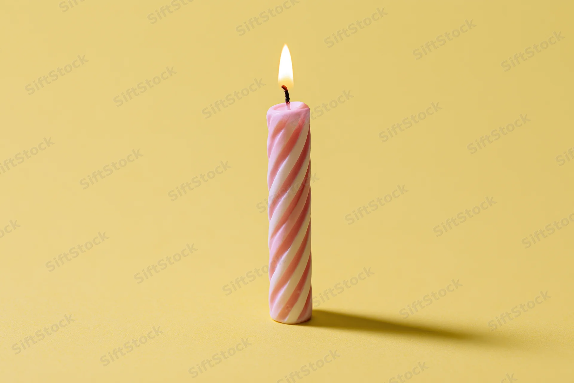 Single lit pink and white spiral birthday candle on yellow background