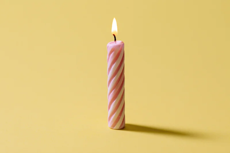 Single lit pink and white spiral birthday candle on yellow background