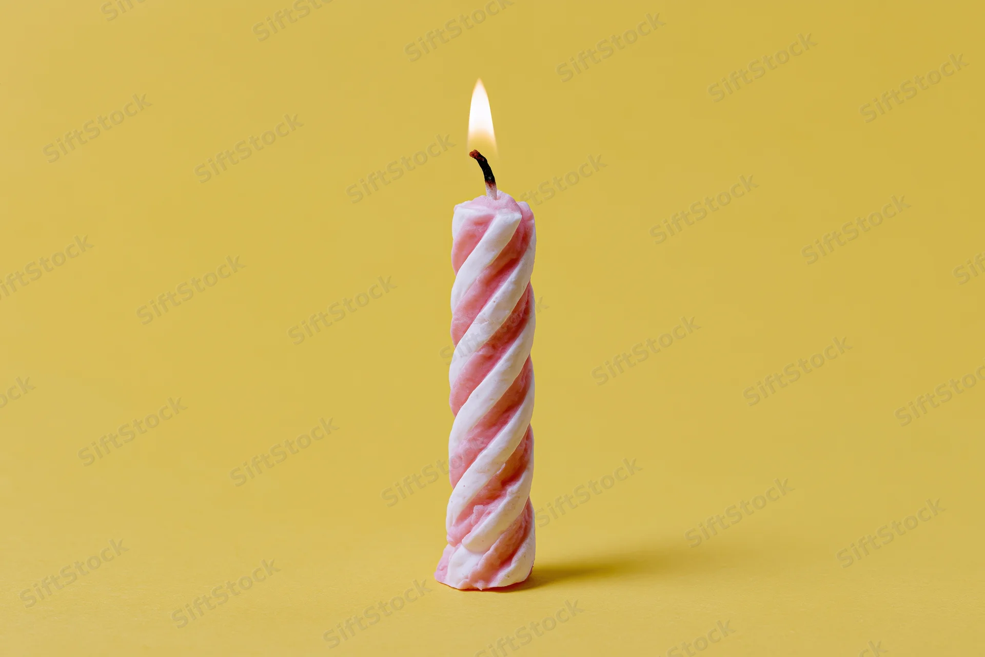 Single lit pink and white spiral birthday candle on yellow background