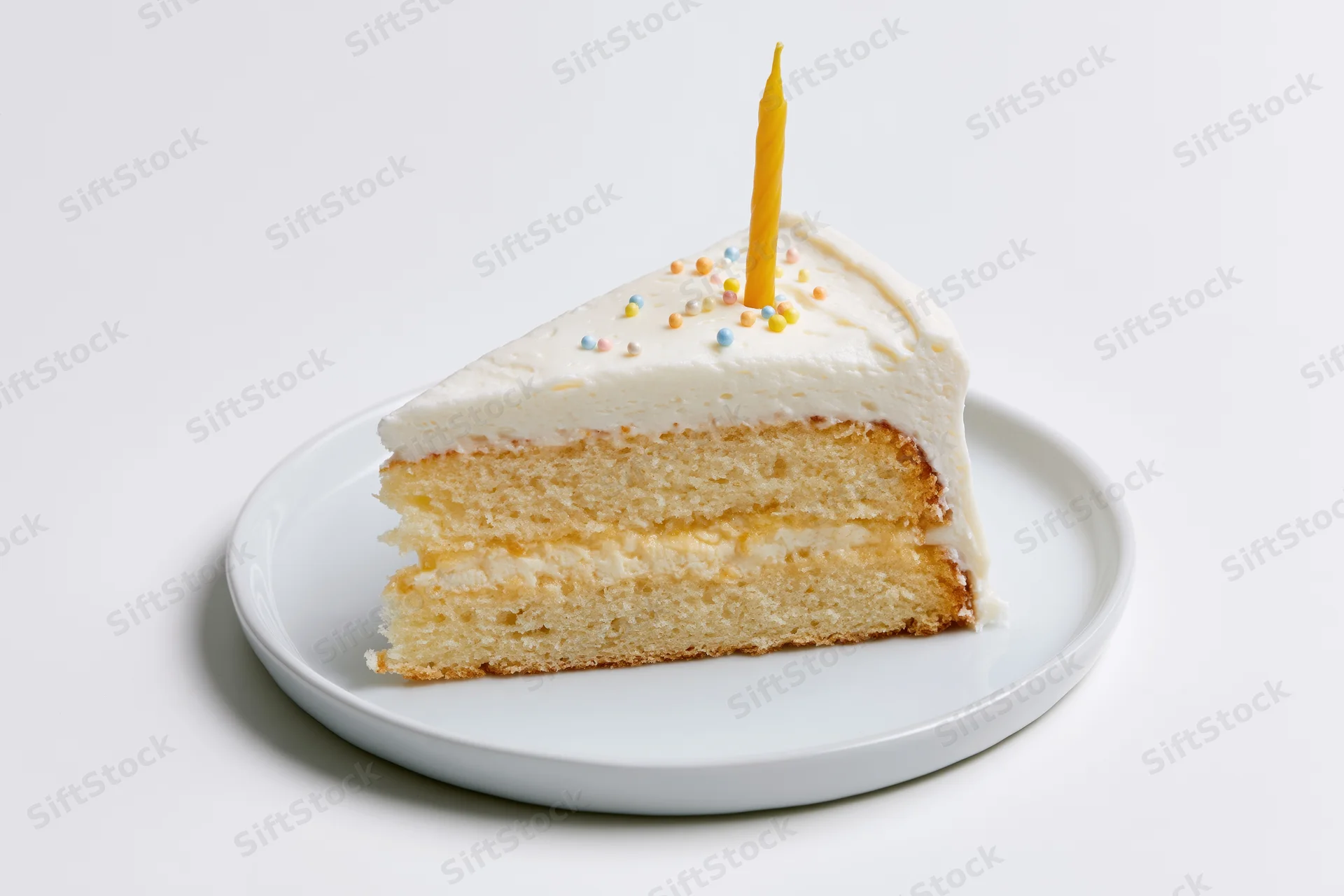 Triangular slice of white-frosted layer birthday cake with yellow candle and sprinkles on white plate