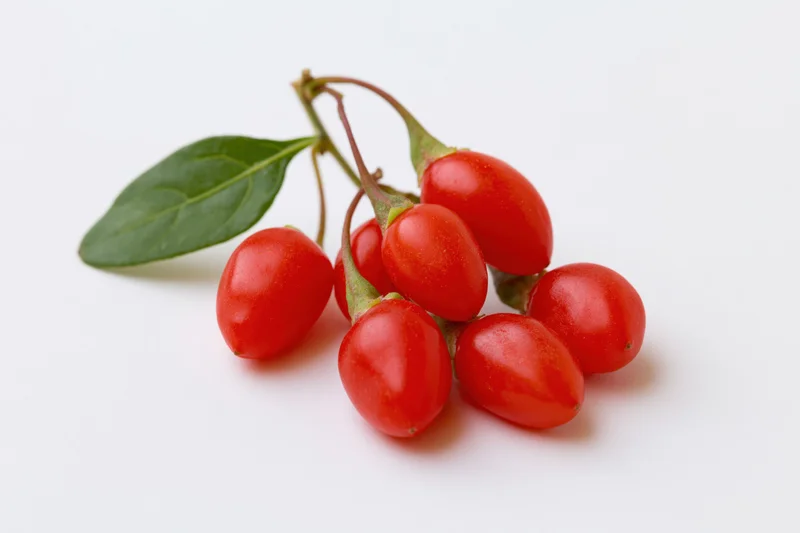 Cluster of fresh red goji berries with stems and a green leaf on white background