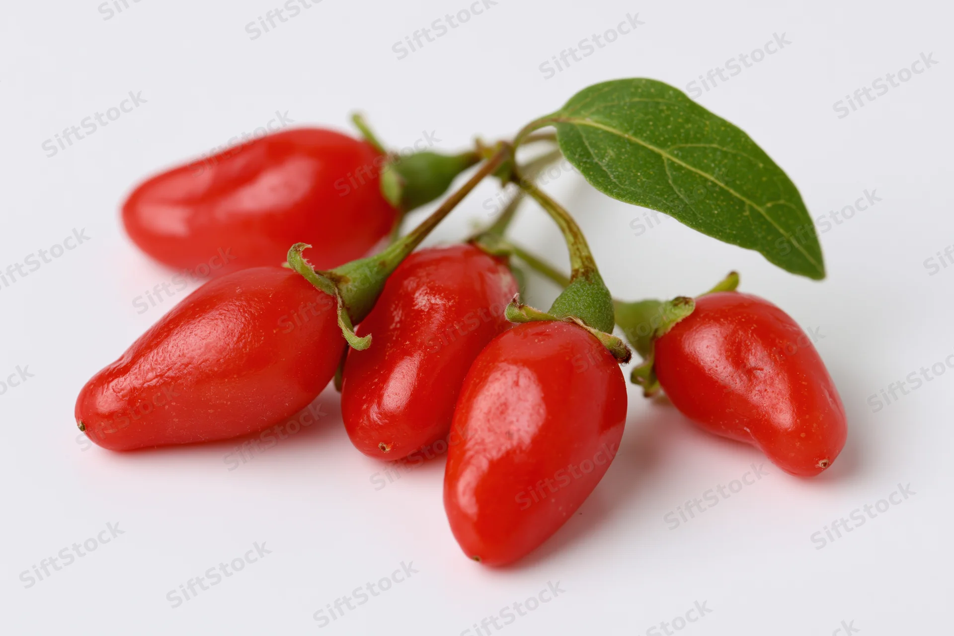 Cluster of fresh red goji berries with stems and a green leaf on white background