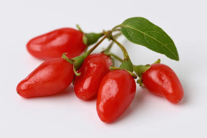 Cluster of fresh red goji berries with stems and a green leaf on white background