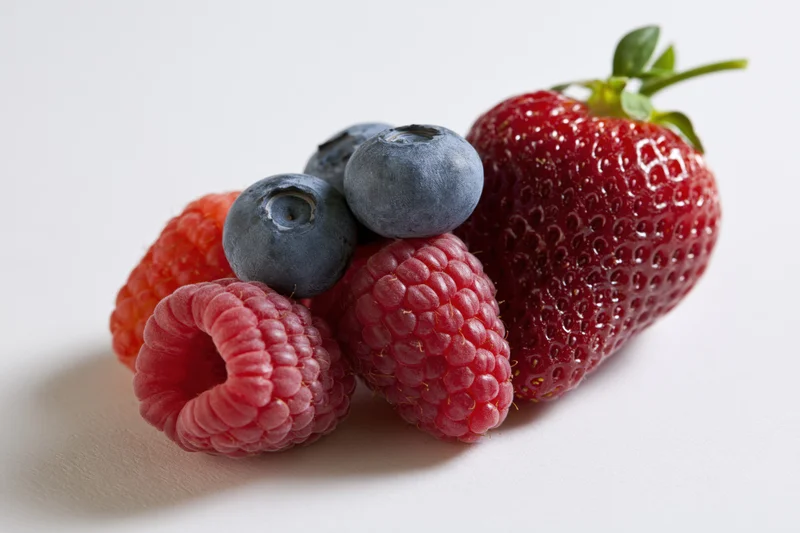 Fresh mixed berries including strawberry raspberry and blueberry arranged on white surface