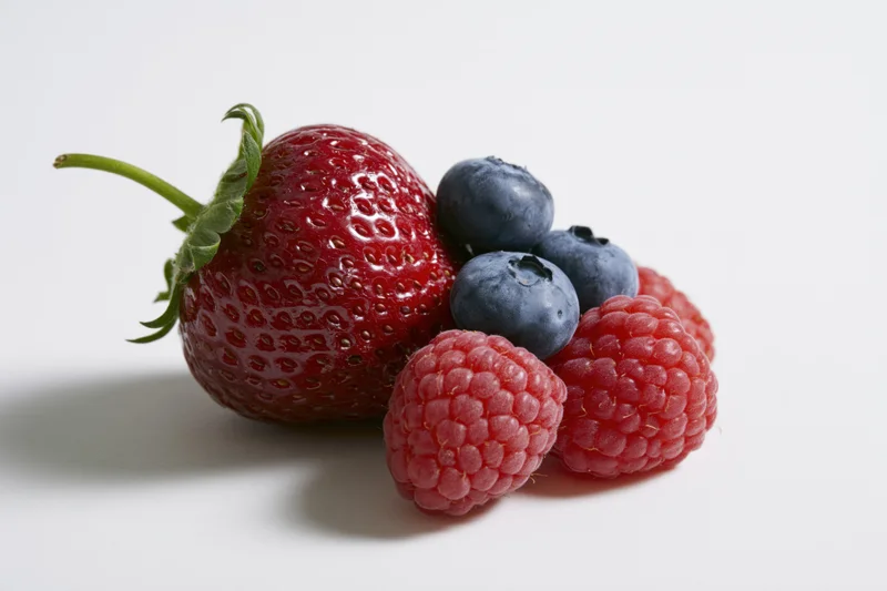 Fresh strawberries, raspberries and blueberries arranged on a white surface