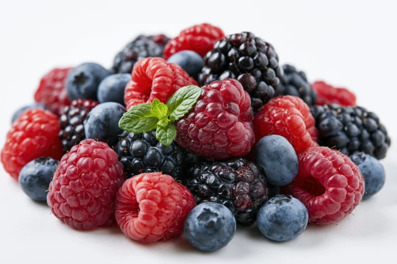 Pile of fresh raspberries, blackberries and blueberries with mint leaves on white background