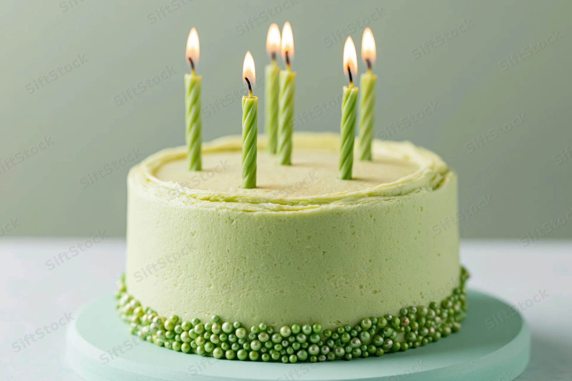 Small round lime green frosted birthday cake with lit candles on a cake stand