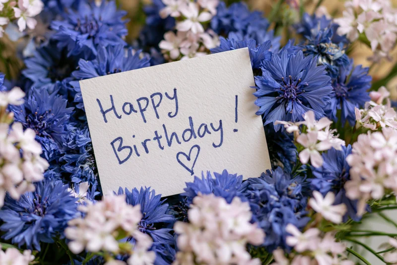 Handwritten birthday card with heart symbol placed among blue and white flowers