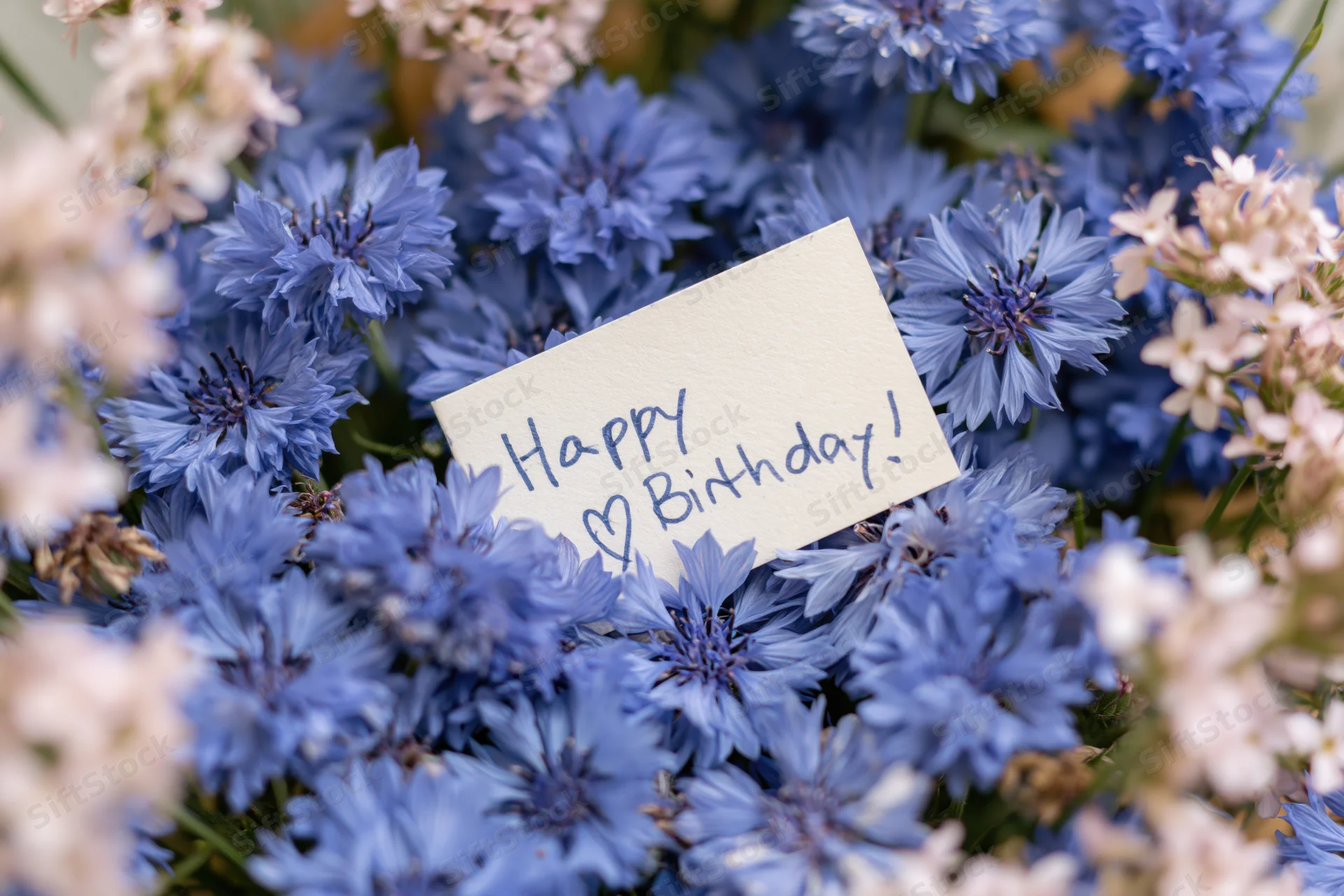 Blue and white flowers arranged in a bouquet with a handwritten birthday card nestled among the blooms
